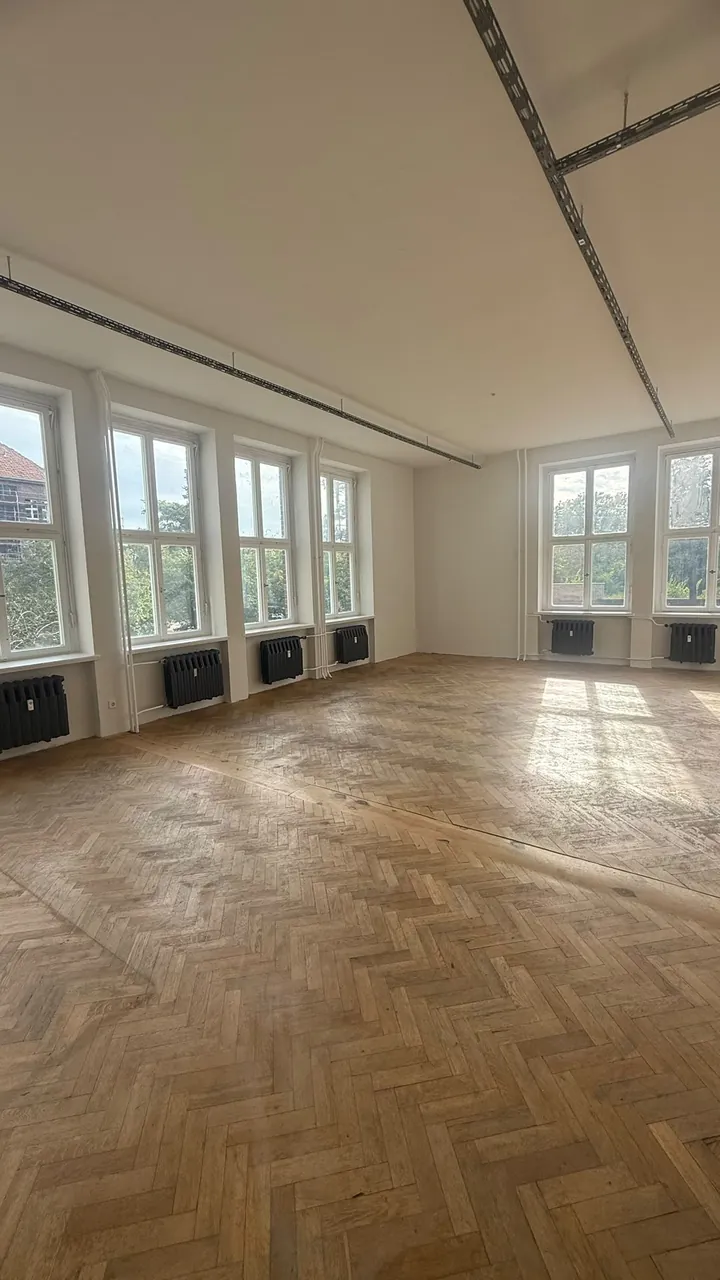 Großer heller Raum mit Fischgrätparkett und Fensterfront nach der Renovierung