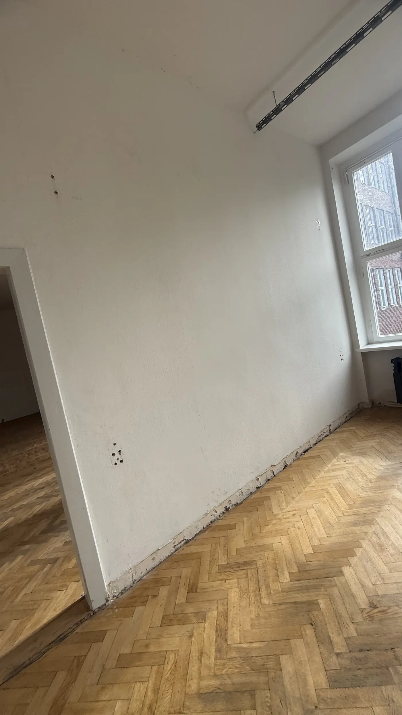 Ausgangszustand: Büroraum mit Fischgrätparkett, Gebrauchsspuren an Wand und Sockelleiste